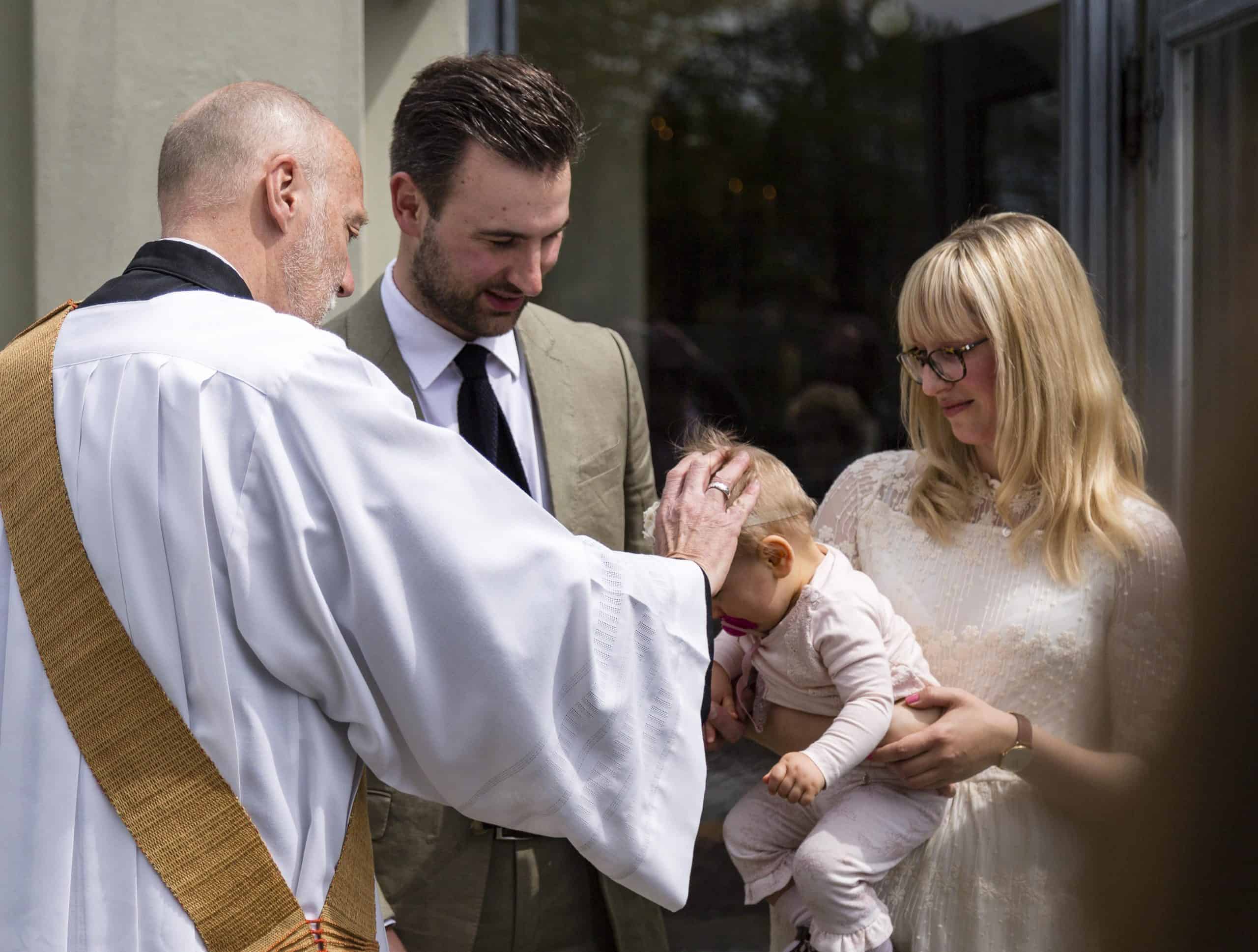 Fotografie Taufe Baby auf Arm der Mutter, Pfarrer legt Hand auf den Kopf auf
